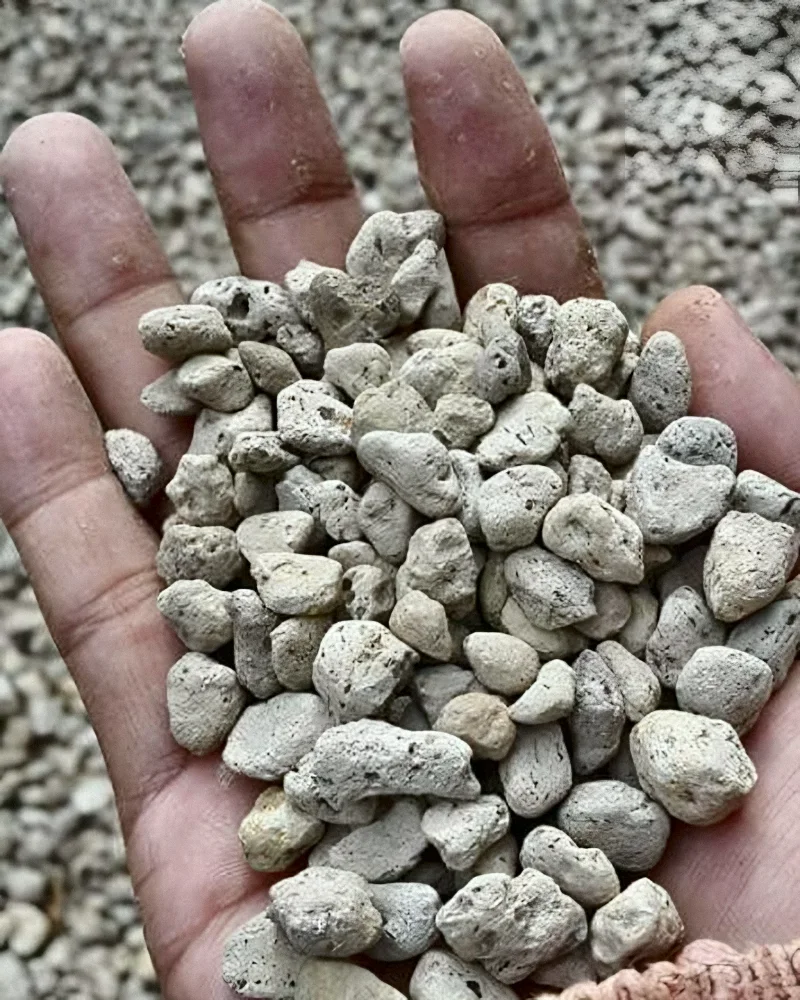 A handful of pumice granules held over a pile of pumice